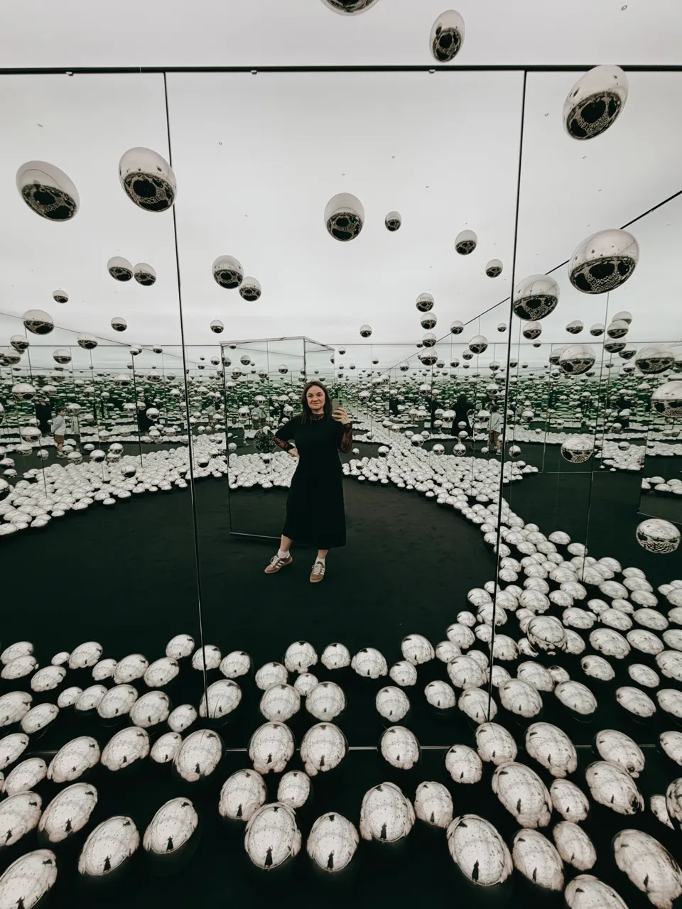 Anastasia standing in a mirrored installation with reflective silver forms.