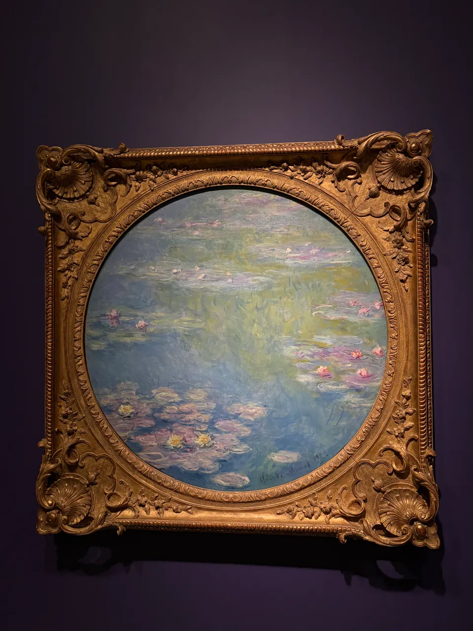 An oval painting of water lilies on a pond.